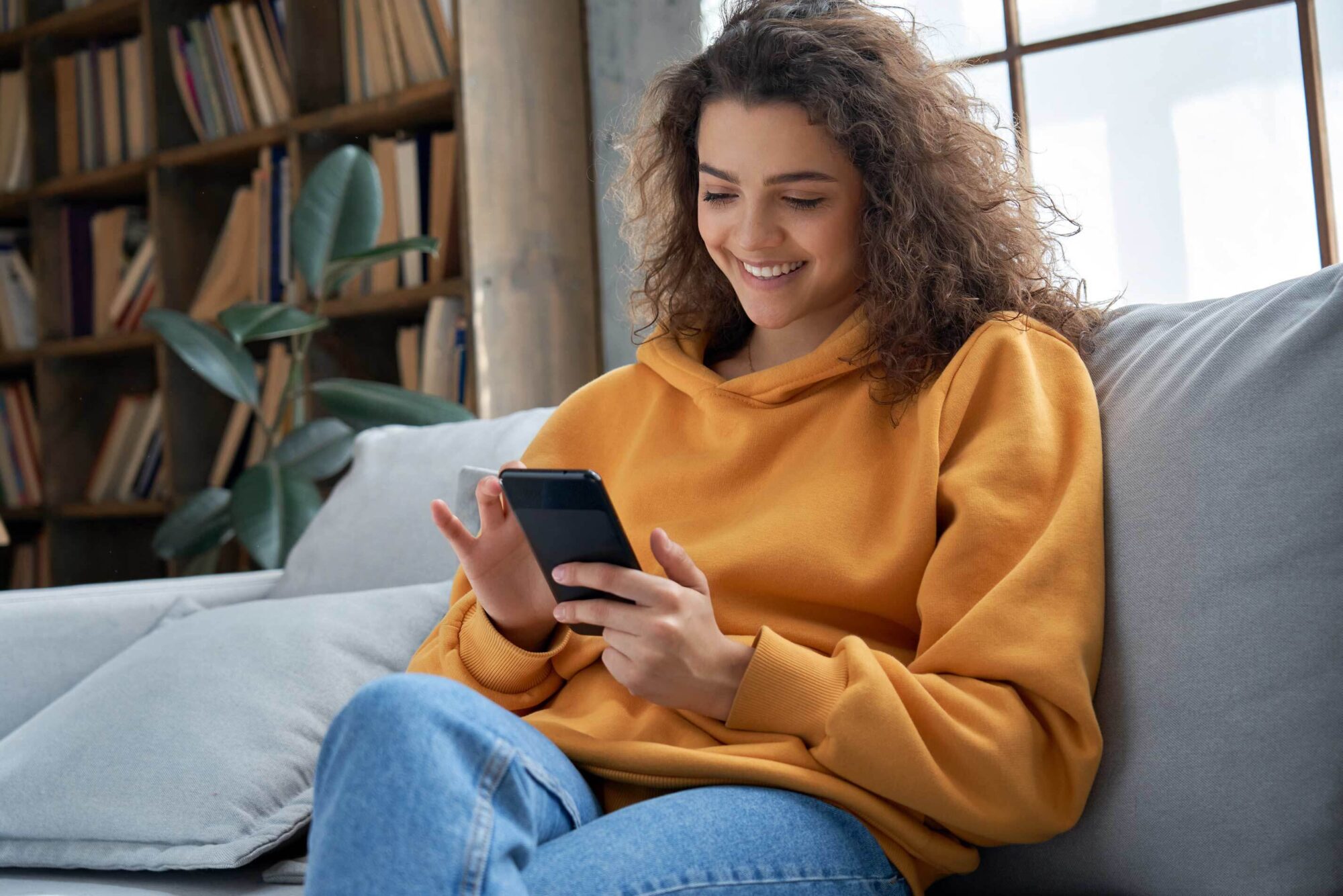 Young woman sitting on a couch smiling at her phone